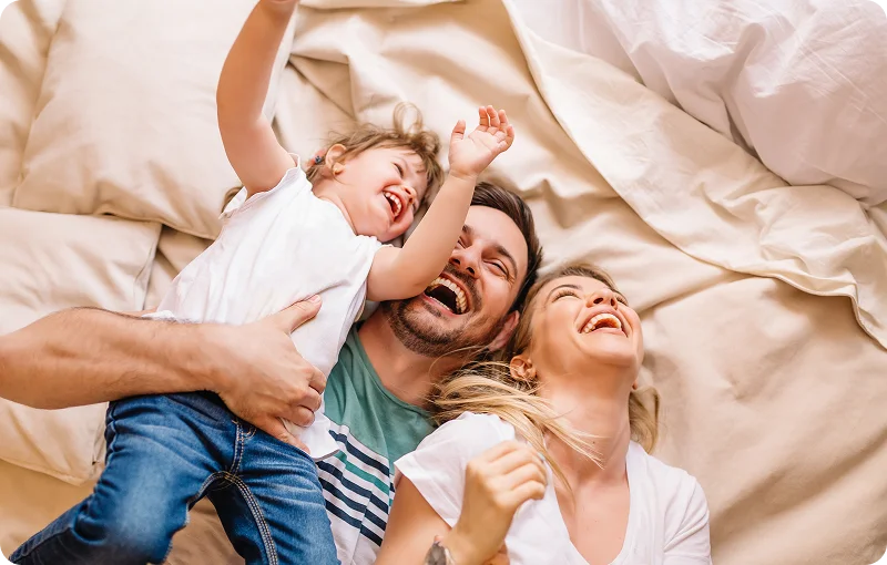 @lang('Família feliz a rir-se e a abraçar-se na cama, já a viver na casa que construiu com o apoio gratuito do Poupança no Minuto.')